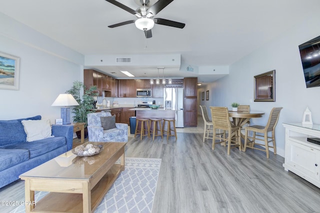 living area featuring baseboards, a ceiling fan, light wood-type flooring, and visible vents