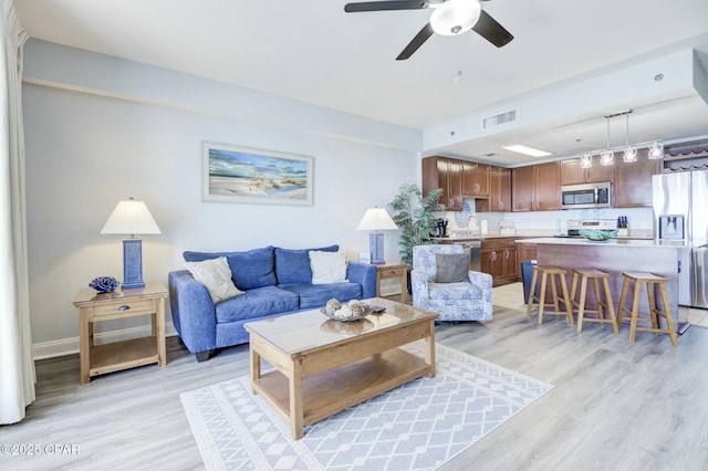 living area featuring baseboards, ceiling fan, light wood finished floors, and visible vents