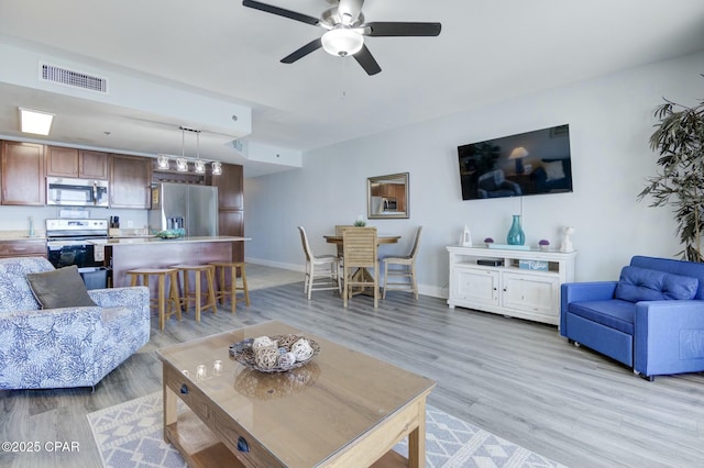 living area featuring baseboards, ceiling fan, light wood-style flooring, and visible vents