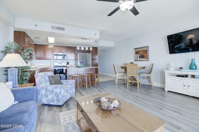 living room featuring visible vents, baseboards, ceiling fan, and light wood finished floors