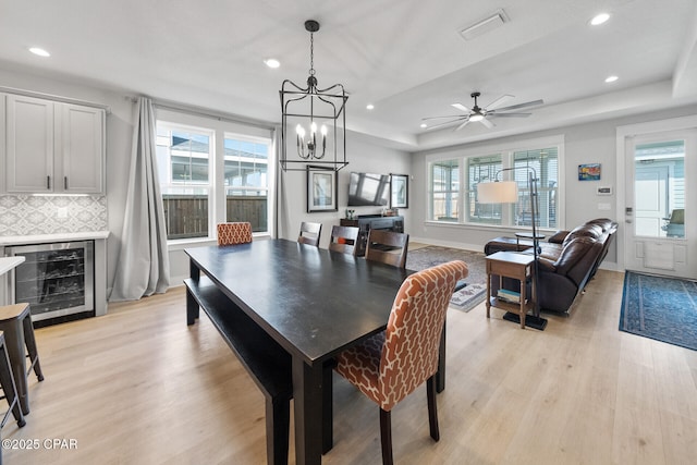 dining room featuring plenty of natural light, beverage cooler, visible vents, a raised ceiling, and light wood-style floors