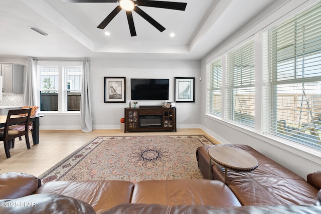 living room featuring a tray ceiling, wood finished floors, visible vents, and baseboards