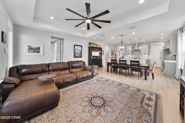 living area with a ceiling fan, a raised ceiling, light wood-style flooring, and recessed lighting