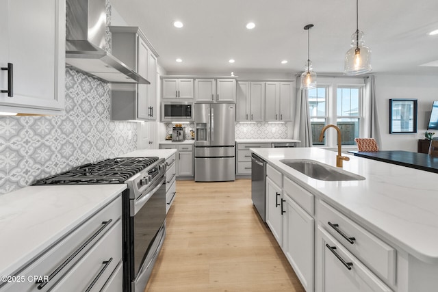 kitchen featuring stainless steel appliances, a sink, hanging light fixtures, light wood-type flooring, and wall chimney exhaust hood