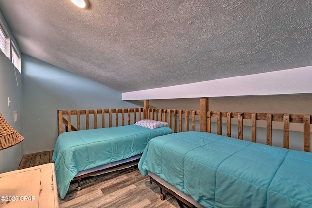 bedroom featuring lofted ceiling, a textured ceiling, and wood finished floors