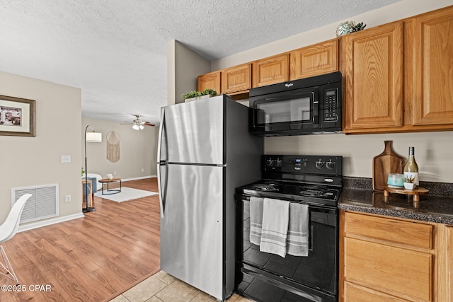 kitchen with visible vents, light wood-style flooring, a textured ceiling, dark stone countertops, and black appliances