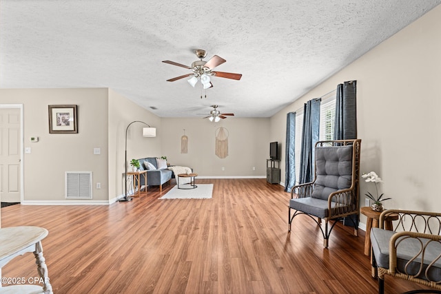 living area with a textured ceiling, ceiling fan, wood finished floors, visible vents, and baseboards