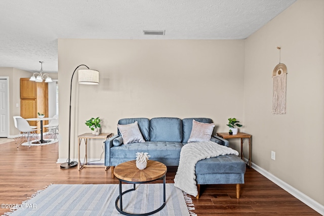 living room featuring an inviting chandelier, a textured ceiling, baseboards, and wood finished floors