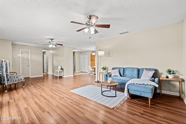 living room featuring a textured ceiling, wood finished floors, visible vents, and baseboards