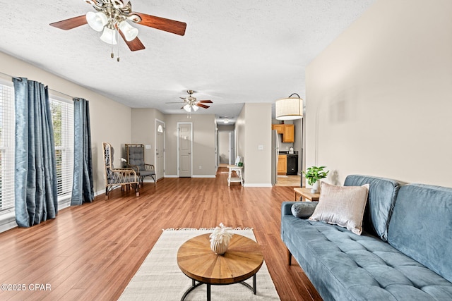 living area with light wood-style floors, ceiling fan, baseboards, and a textured ceiling