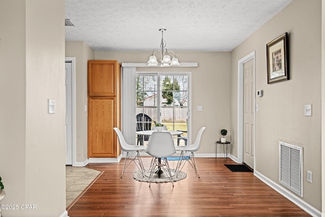 dining room featuring a textured ceiling, a notable chandelier, wood finished floors, visible vents, and baseboards