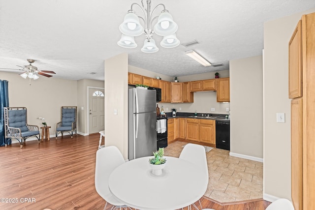 kitchen with light wood-style flooring, a sink, black dishwasher, freestanding refrigerator, and dark countertops