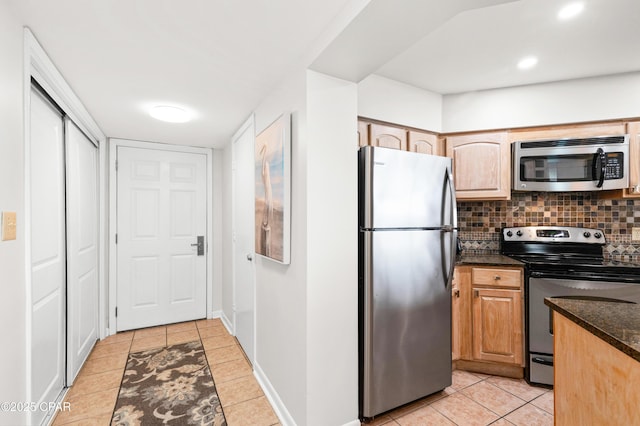 kitchen with appliances with stainless steel finishes, dark stone counters, light tile patterned flooring, and tasteful backsplash