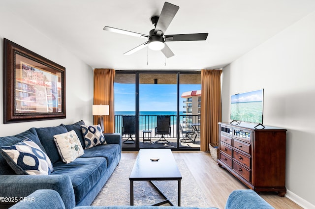 living room featuring light wood finished floors, baseboards, a wall of windows, and a ceiling fan