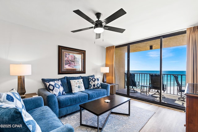 living room with a wall of windows, a water view, wood finished floors, and a ceiling fan