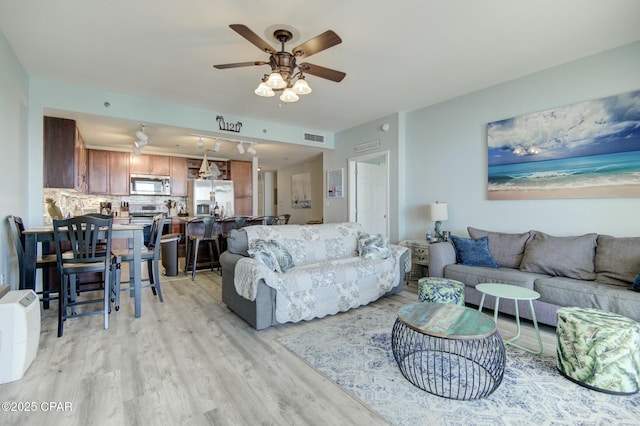 living area featuring light wood-type flooring, visible vents, and a ceiling fan