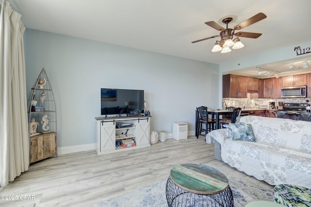 living area featuring light wood finished floors, baseboards, and a ceiling fan