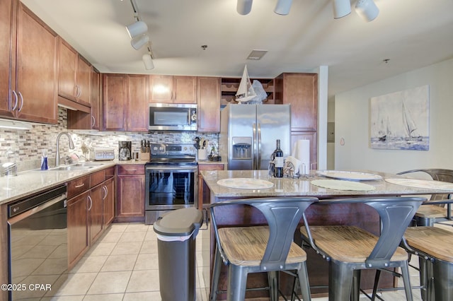 kitchen with light tile patterned floors, light stone counters, stainless steel appliances, a kitchen breakfast bar, and backsplash