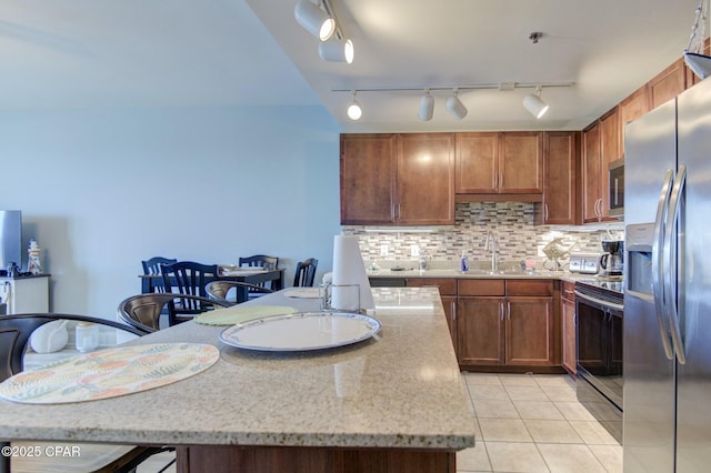 kitchen with light tile patterned floors, tasteful backsplash, appliances with stainless steel finishes, light stone counters, and a sink