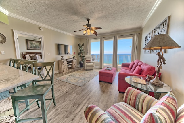 living area with ceiling fan, a textured ceiling, ornamental molding, and wood finished floors