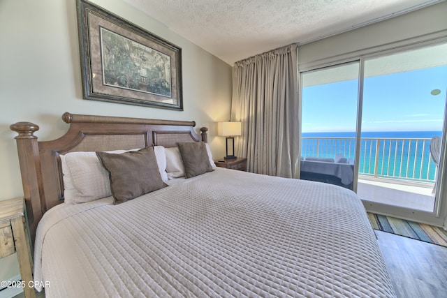 bedroom with a water view, a textured ceiling, and wood finished floors