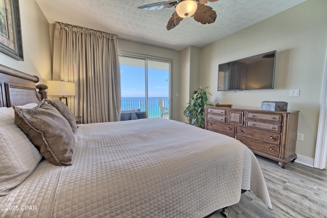 bedroom with a textured ceiling, wood finished floors, a ceiling fan, baseboards, and access to outside