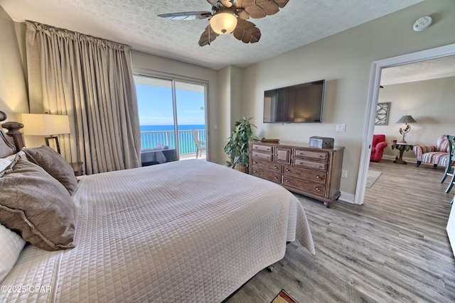 bedroom featuring access to exterior, a textured ceiling, baseboards, and wood finished floors