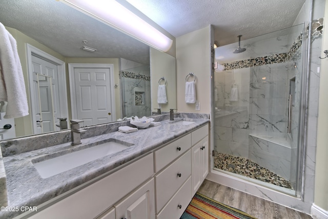 full bathroom with double vanity, a sink, a marble finish shower, and wood finished floors