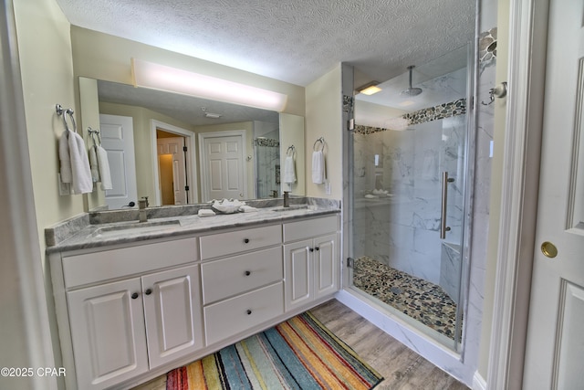 bathroom with a marble finish shower, double vanity, a sink, a textured ceiling, and wood finished floors