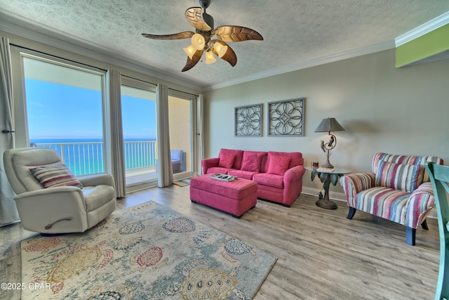 living area featuring baseboards, ornamental molding, wood finished floors, a water view, and a textured ceiling