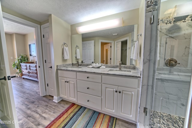 bathroom featuring double vanity, a marble finish shower, wood finished floors, a textured ceiling, and a sink