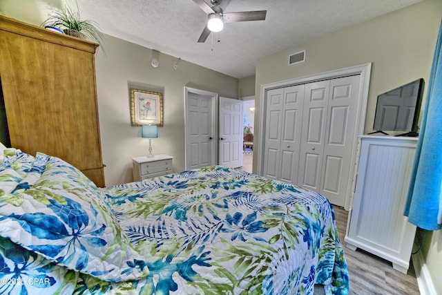 bedroom with a textured ceiling, ceiling fan, wood finished floors, visible vents, and a closet