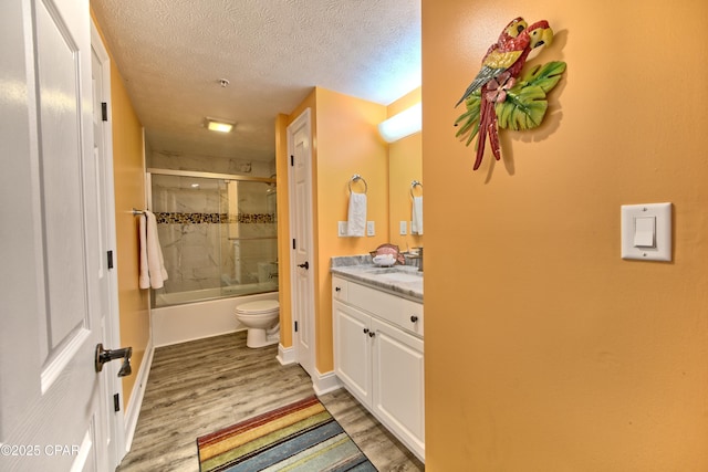 full bathroom featuring a textured ceiling, enclosed tub / shower combo, toilet, wood finished floors, and vanity