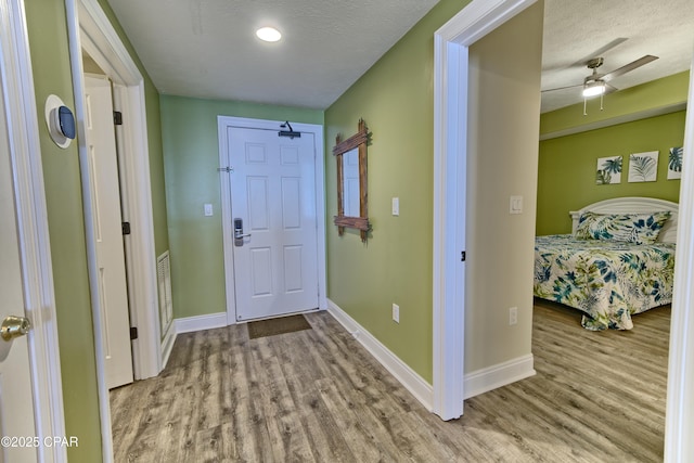 hall with a textured ceiling, baseboards, and wood finished floors