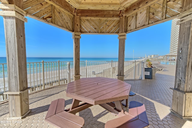 view of patio with a beach view, a water view, and a gazebo