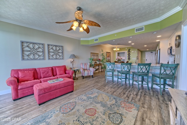 living area featuring crown molding, a textured ceiling, visible vents, and wood finished floors