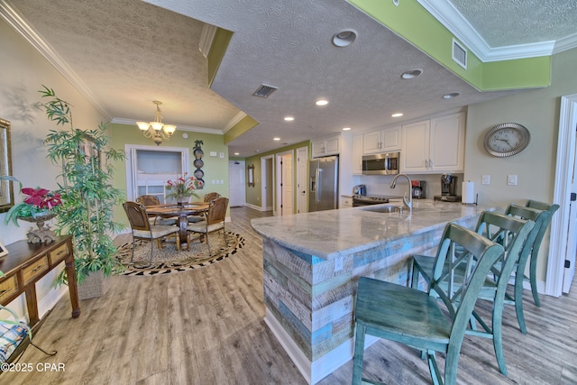 kitchen featuring stainless steel appliances, a peninsula, a sink, visible vents, and white cabinetry