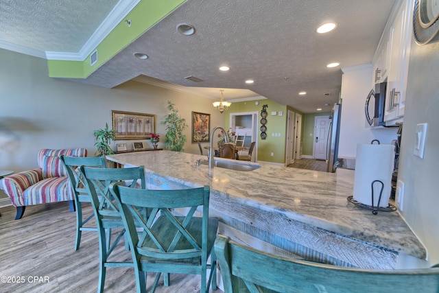 kitchen with light wood-type flooring, white cabinetry, stainless steel microwave, and a sink