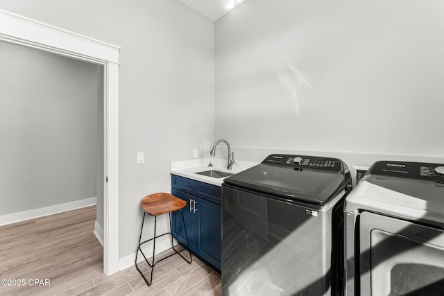 clothes washing area with independent washer and dryer, baseboards, cabinet space, a sink, and light wood-type flooring