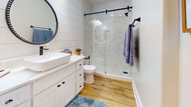 full bath with toilet, wooden walls, wood finished floors, vanity, and a marble finish shower