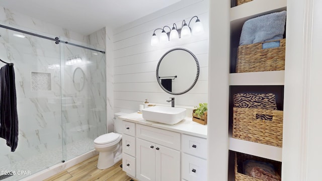 full bath with a marble finish shower, toilet, wood walls, vanity, and wood finished floors