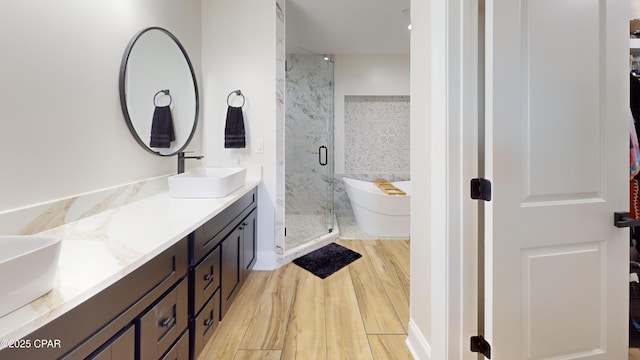 bathroom with double vanity, a stall shower, wood finished floors, a freestanding bath, and a sink