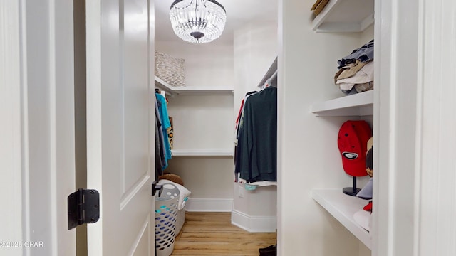 spacious closet featuring light wood-type flooring and a notable chandelier