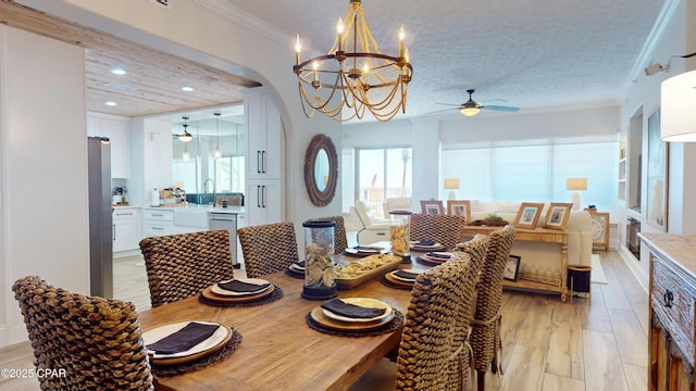 dining room with light wood finished floors, arched walkways, ornamental molding, ceiling fan with notable chandelier, and recessed lighting