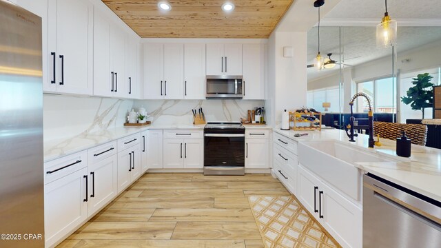 kitchen featuring white cabinets, hanging light fixtures, appliances with stainless steel finishes, light wood-type flooring, and decorative backsplash