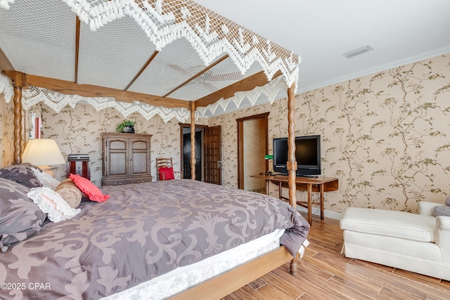 bedroom featuring wallpapered walls, baseboards, visible vents, ornamental molding, and wood finished floors