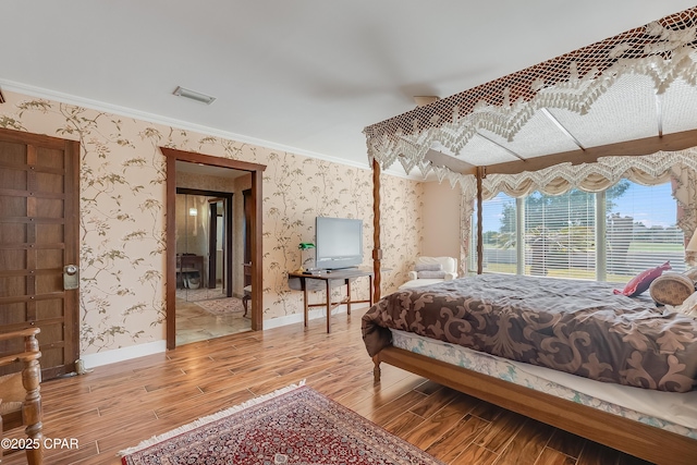 bedroom with crown molding, wood finished floors, visible vents, and wallpapered walls