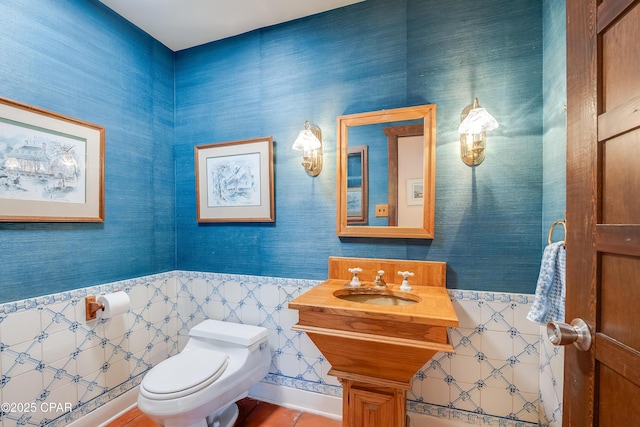 half bath featuring a sink, toilet, and wallpapered walls