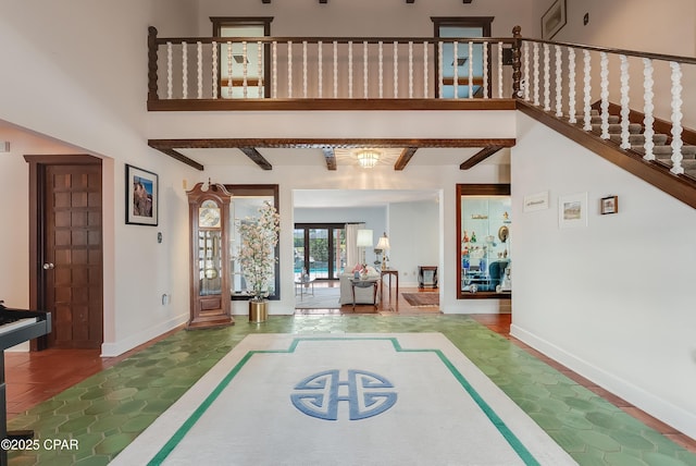 foyer featuring a towering ceiling, beam ceiling, and baseboards