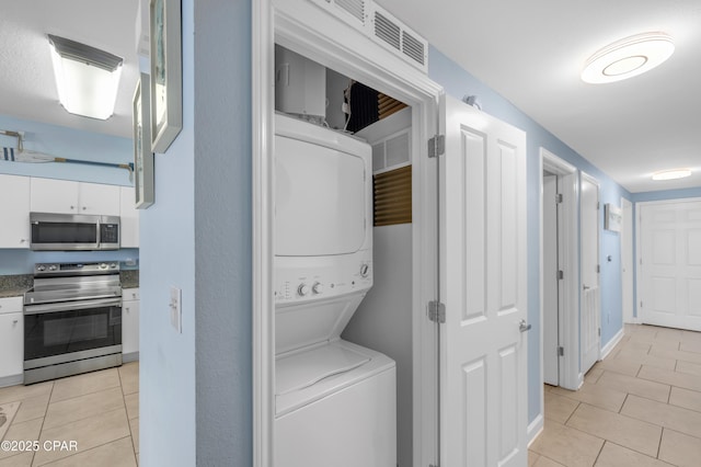 washroom featuring stacked washer / drying machine, laundry area, light tile patterned flooring, and baseboards